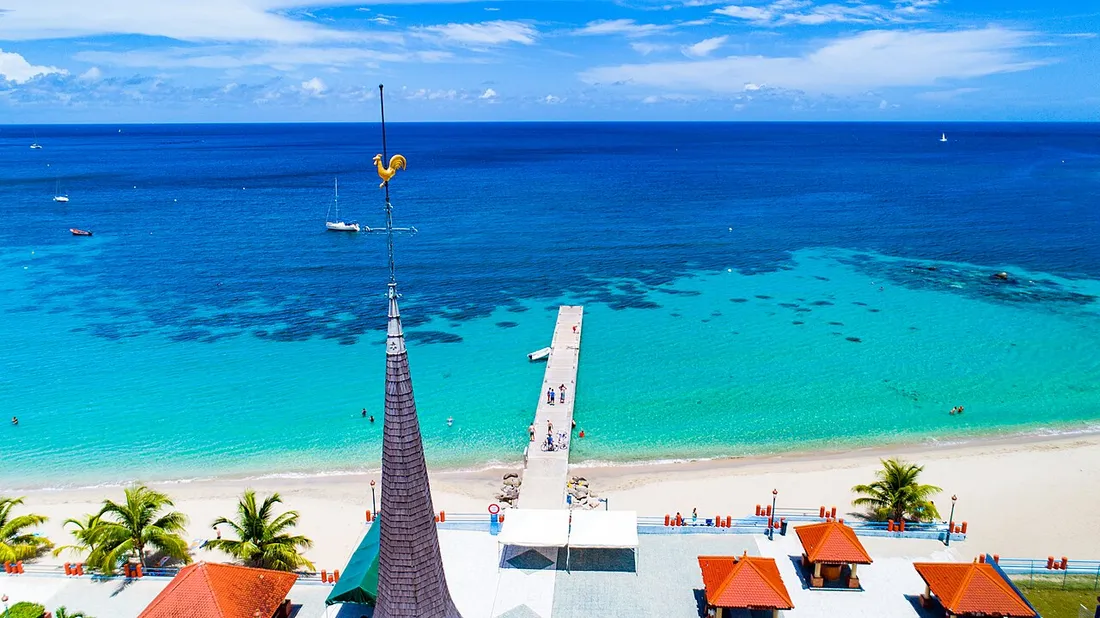 Vue aérienne de la plage des Anses-d'Arlet en Martinique, avec le ponton public avançant dans l'eau turquoise devant l'église du bourg
