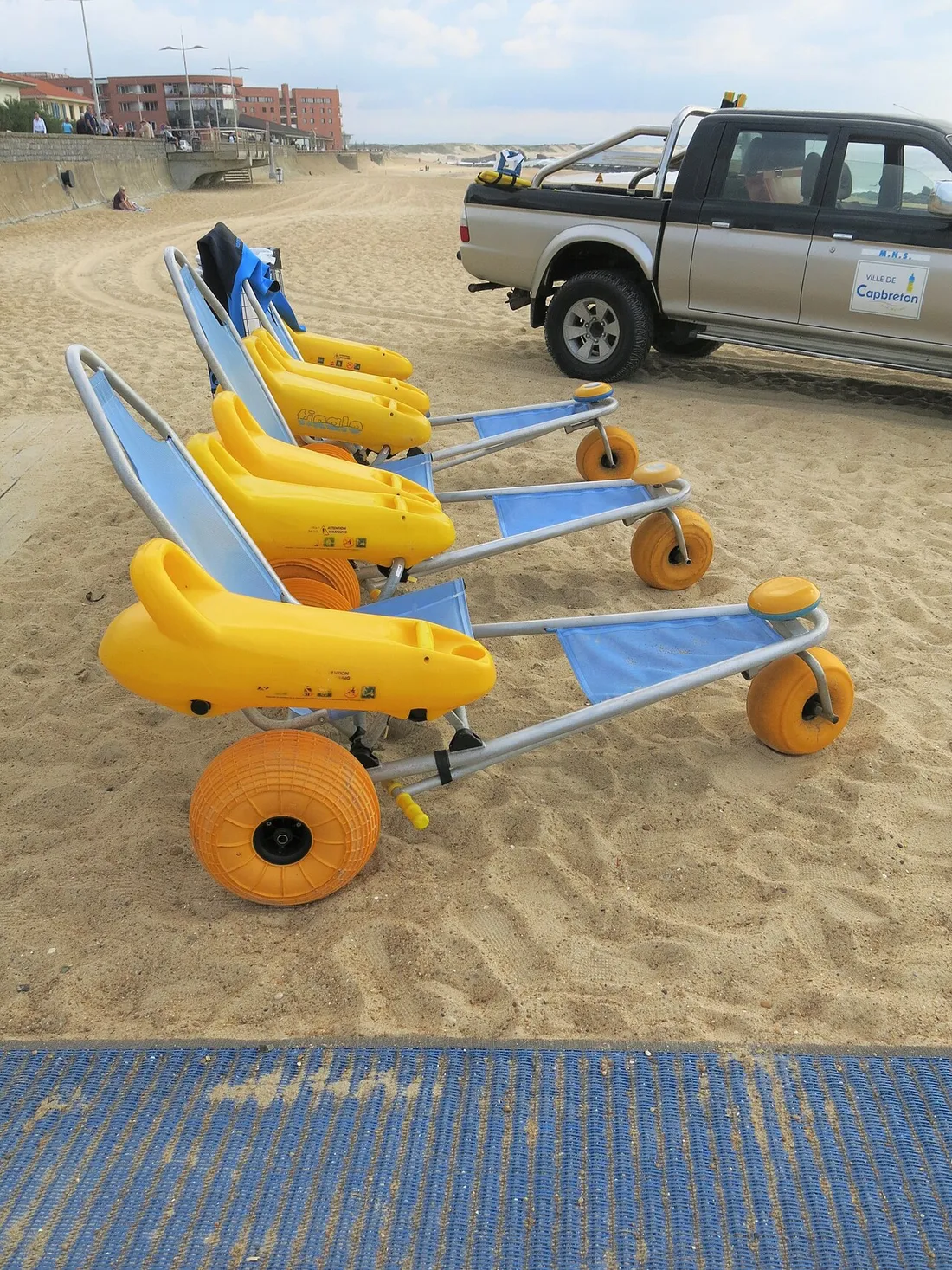 Fauteuils amphibies Tiralo jaunes alignes sur le sable au bord d'un tapis d'acces PMR sur une plage