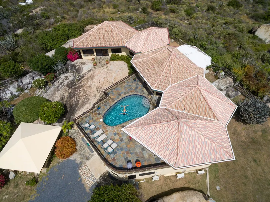 Vue aérienne d'une villa antillaise avec piscine et toiture en tuiles, entourée de végétation tropicale