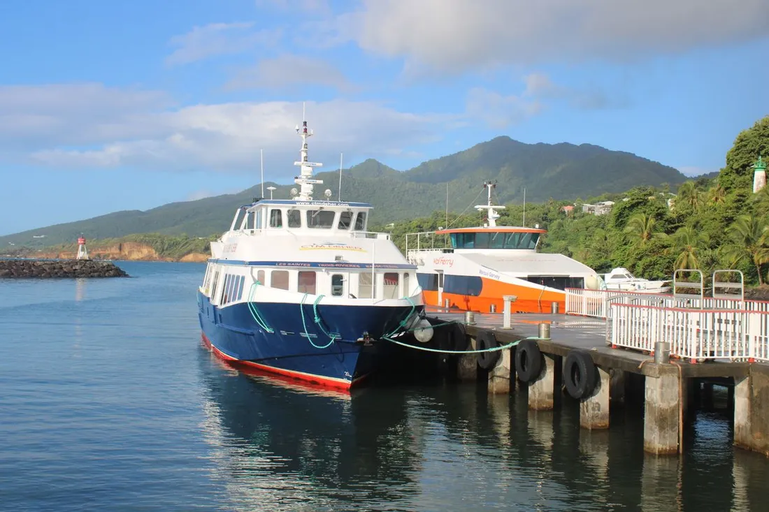Navette maritime des Saintes amarrée au ponton, coque marquée Les Saintes - Trois-Rivières, devant les mornes de la Basse-Terre en Guadeloupe