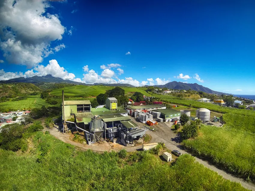 Vue aérienne de la distillerie de rhum Bologne en Guadeloupe, entourée de champs de canne à sucre au pied de la Soufrière