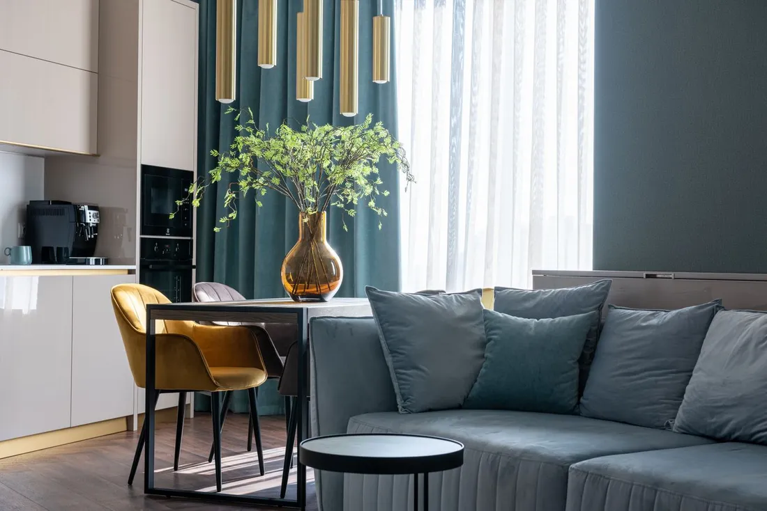 Salon lumineux d'un appartement meublé moderne avec canapé, coin repas et cuisine équipée (machine à café, four)