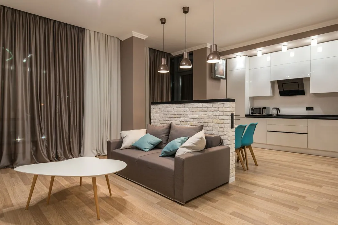 Espace de vie ouvert d'un appartement meublé avec canapé, table basse et cuisine intégrée en enfilade