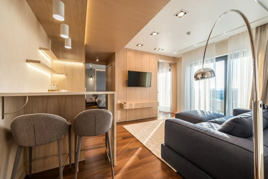 Séjour d'un appart-hôtel : salon avec canapé, téléviseur et coin cuisine équipé avec bar et tabourets
