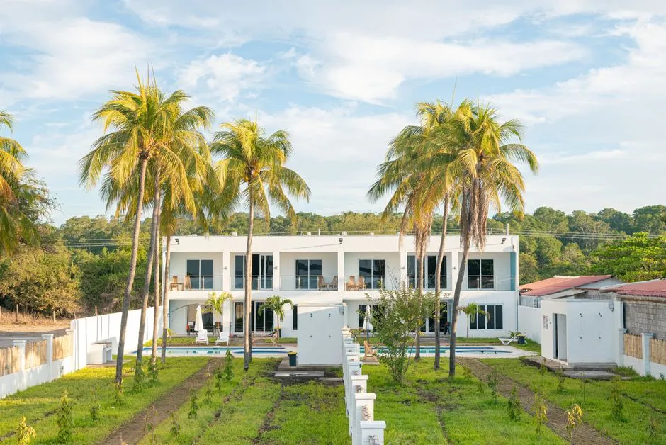 Villa de location saisonniere blanche entouree de palmiers et de pelouse sous un ciel tropical
