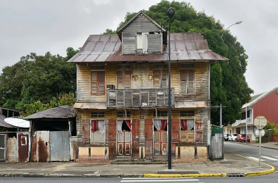 Maison créole en bois vieillissante à Cayenne en Guyane, toiture en tôle rouillée et façade dégradée par l'humidité tropicale