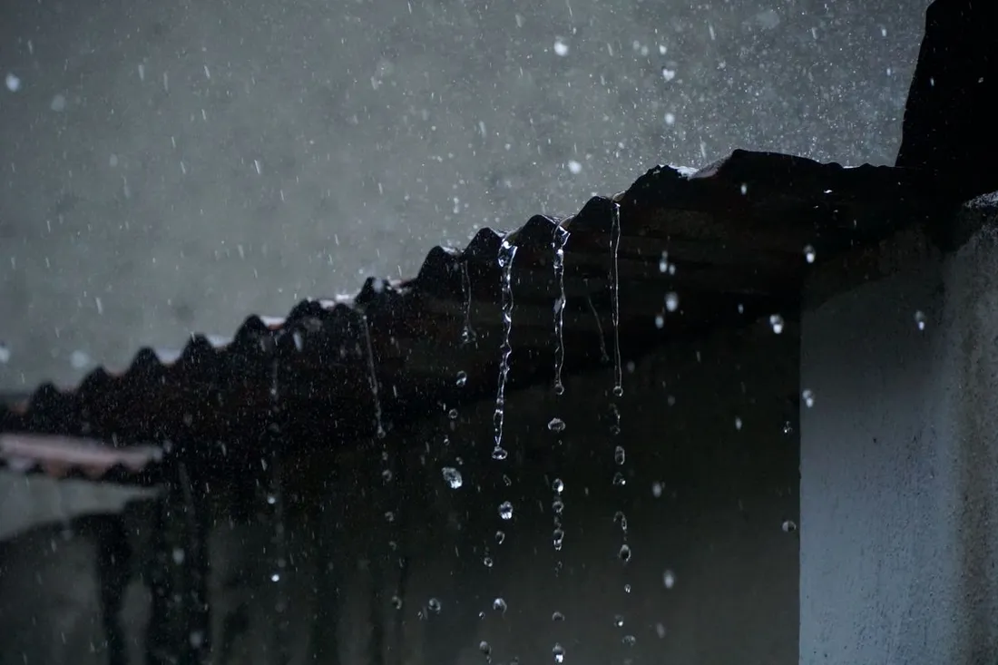 Forte pluie tropicale ruisselant en cascade depuis le bord d'une toiture en tôle ondulée pendant la saison des pluies