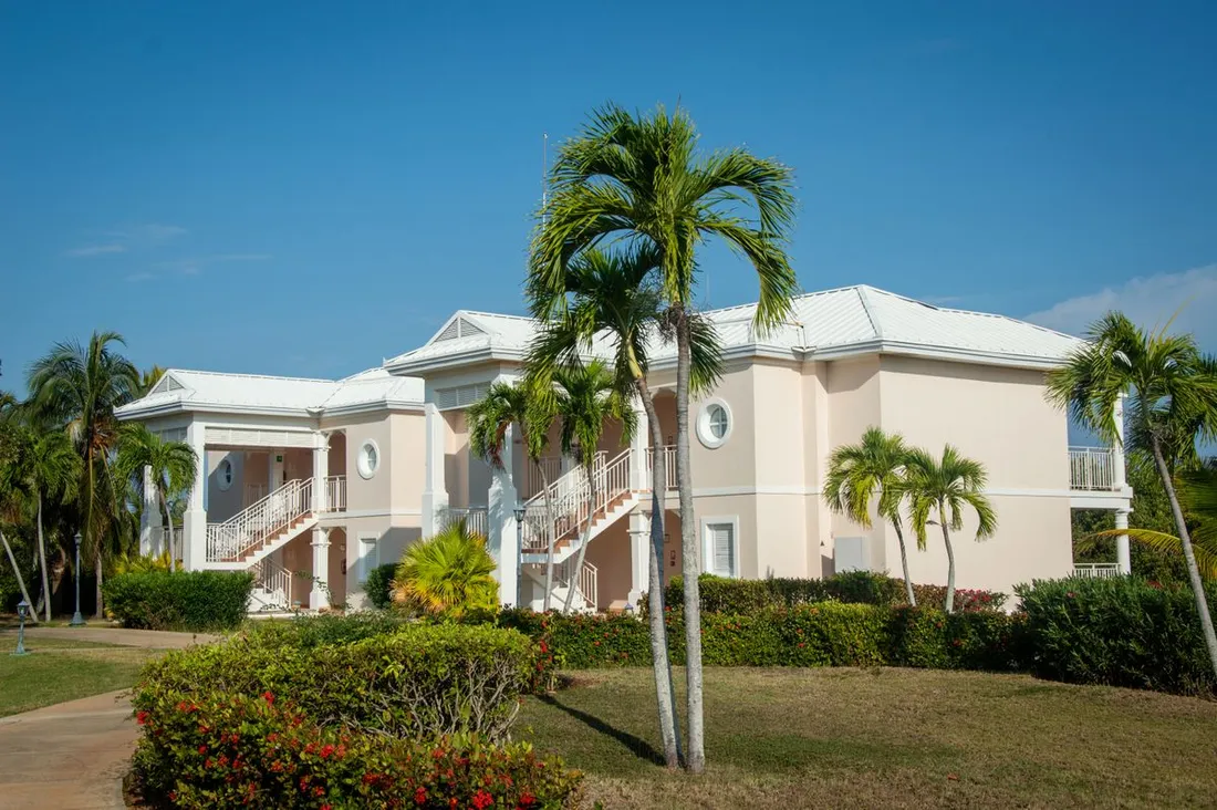 Villa de location saisonniere de style antillais entouree de palmiers sous un ciel bleu, typique d'un hebergement Airbnb a assurer aux Caraibes