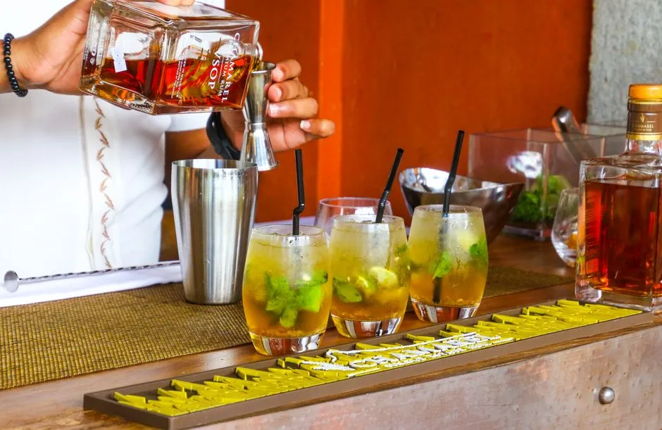 Personne versant du rhum au doseur pour preparer des verres garnis de menthe fraiche et de citron vert lors d'un atelier de degustation