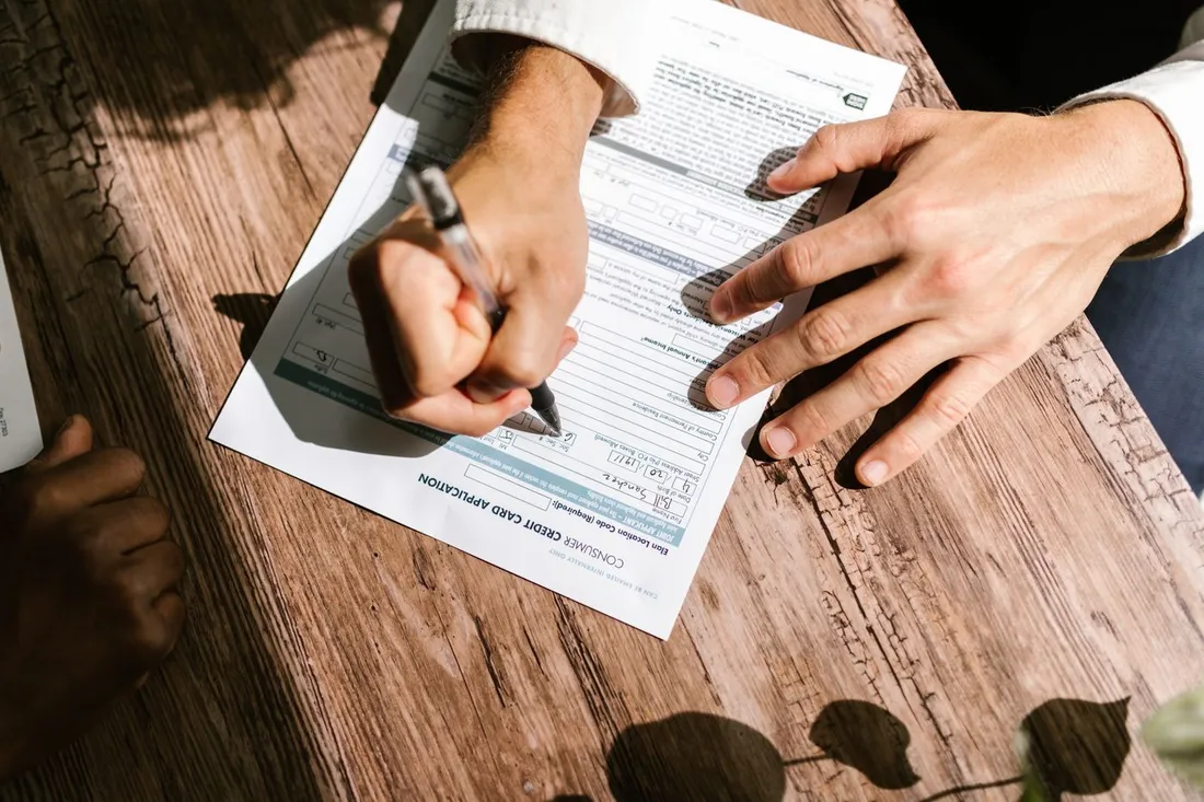 Deux personnes remplissant un formulaire d'ouverture de compte bancaire sur une table en bois, stylo a la main