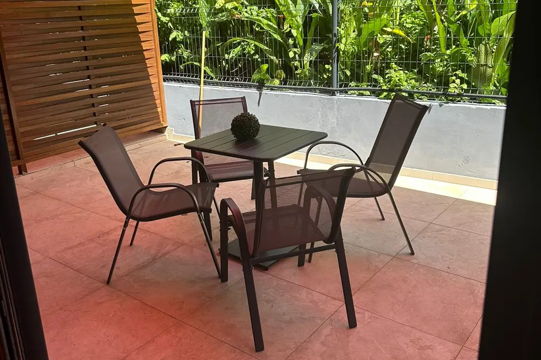 Terrasse carrelée d’un logement de la Résidence Francis : table et quatre chaises devant la végétation
