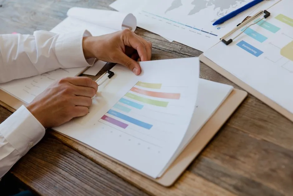 Mains d'un professionnel analysant un rapport imprimé avec des graphiques en barres colorés, stylo à la main, sur un bureau en bois