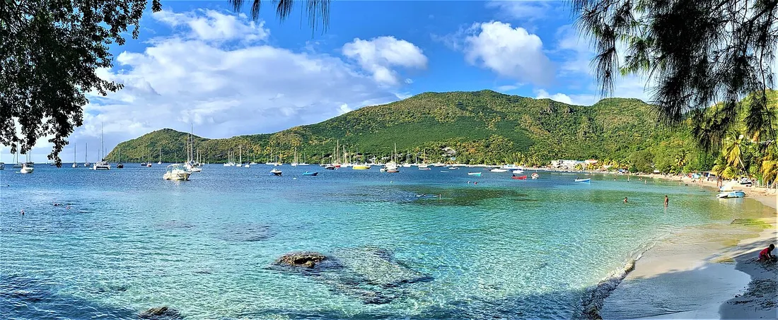 Baie de Grand Anse aux Anses-d'Arlet en Martinique par temps clair, eau turquoise, voiliers et collines verdoyantes, contraste avec un sejour perturbe par la brume de sable