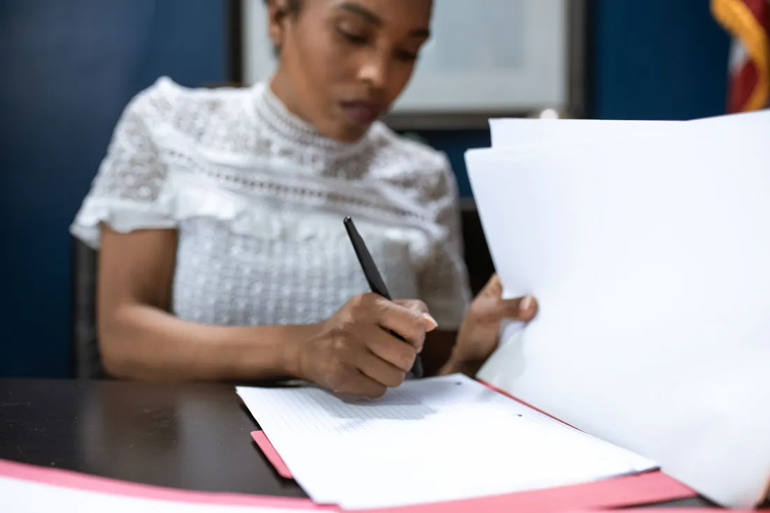 Personne assise à un bureau administratif remplissant et signant des documents papier
