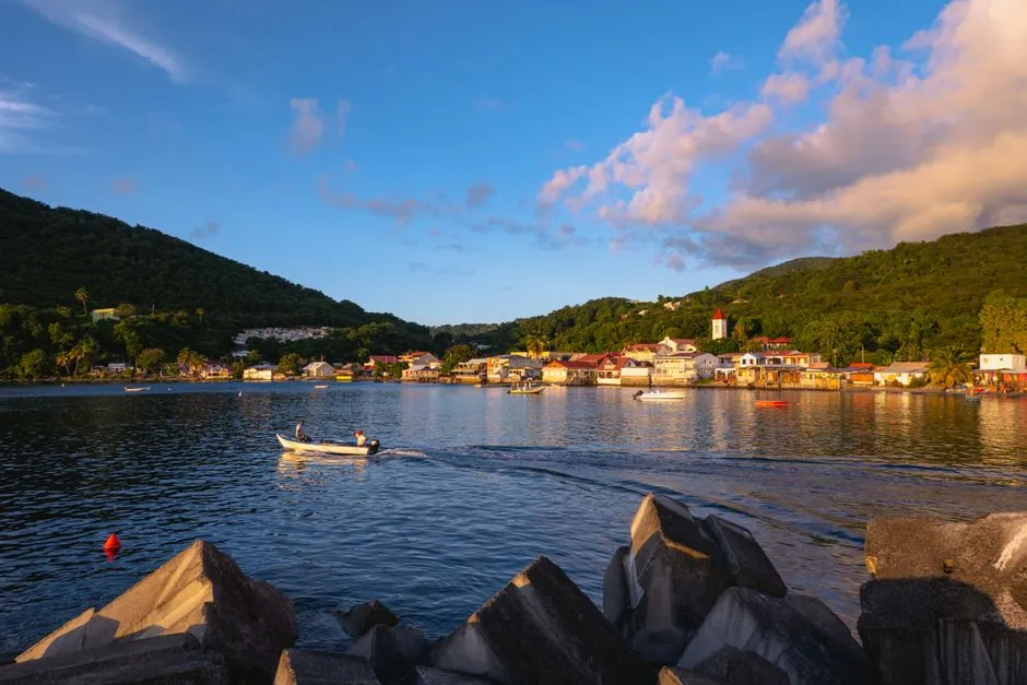La baie de Deshaies au coucher du soleil en Guadeloupe, avec ses maisons en bord de mer et une barque de pecheur