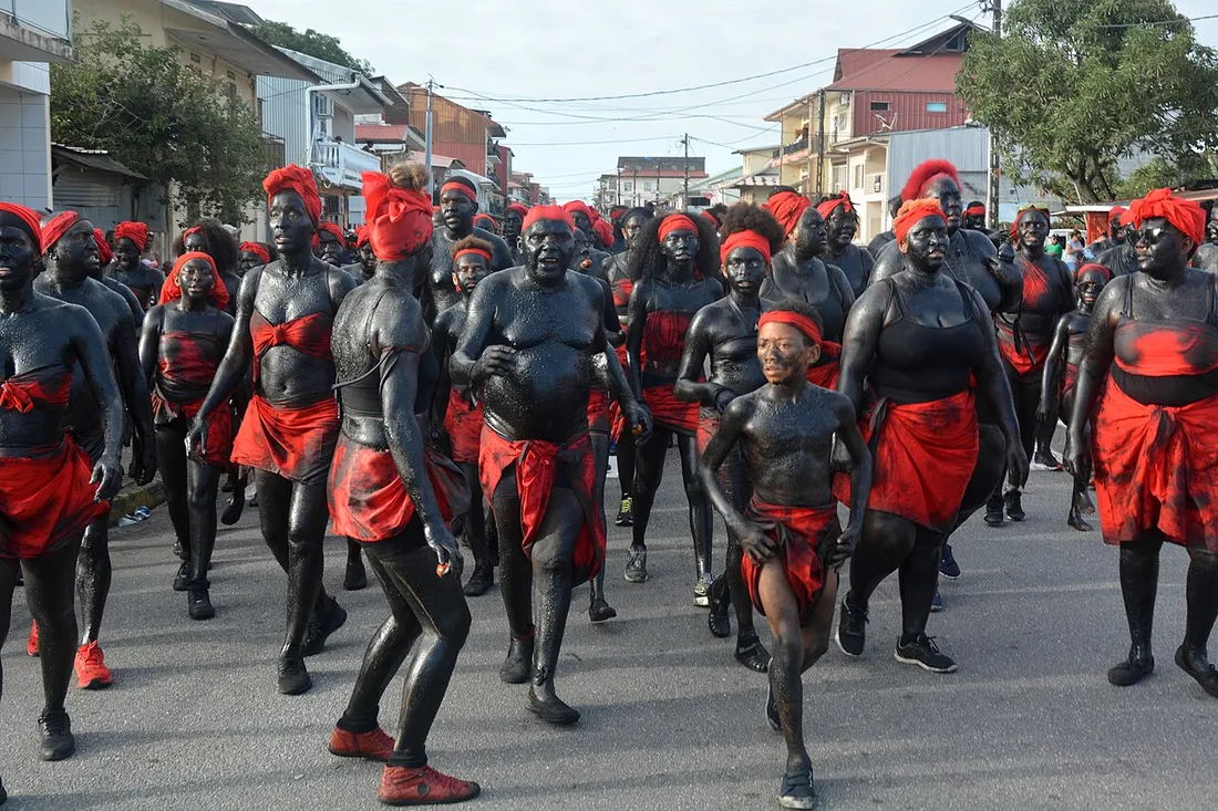 Groupe de nèg marrons au corps peint en noir et pagne rouge défilant dans une rue de Cayenne lors du carnaval guyanais 2024