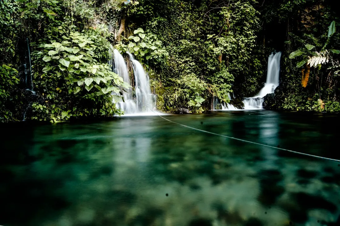 Bassin naturel d'eau turquoise alimente par de petites cascades en pleine foret tropicale, evoquant un spot de baignade nature comme la cascade de Fourgassie a Roura