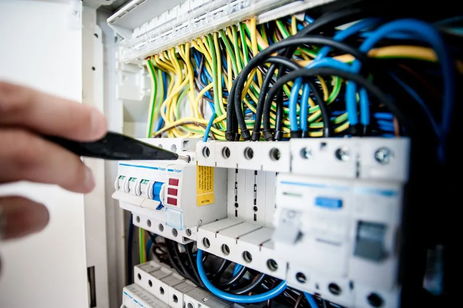 Main intervenant sur un tableau electrique avec disjoncteurs et cablage, illustrant le poste electricite des charges d'un meuble