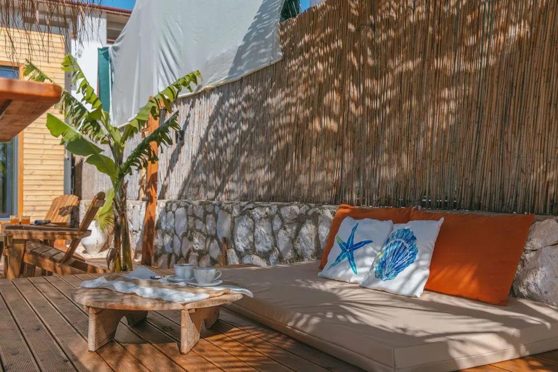 Terrasse en bois d'un hébergement de location de vacances aux Antilles, banquette avec coussins décor coquillages