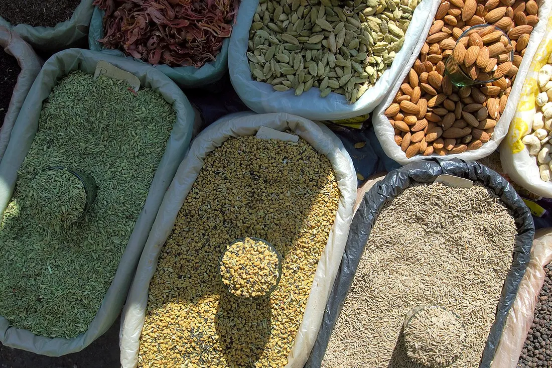 Etals de marche indien presentant des epices, graines et amandes en vrac, dont la cardamome et le fenugrec qui composent la poudre de colombo
