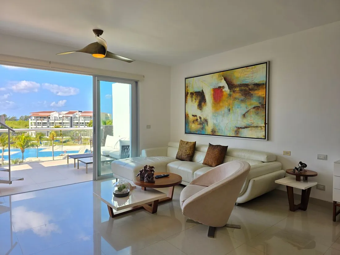 Salon d'un appartement meuble moderne ouvert sur un balcon avec vue piscine et mer tropicale