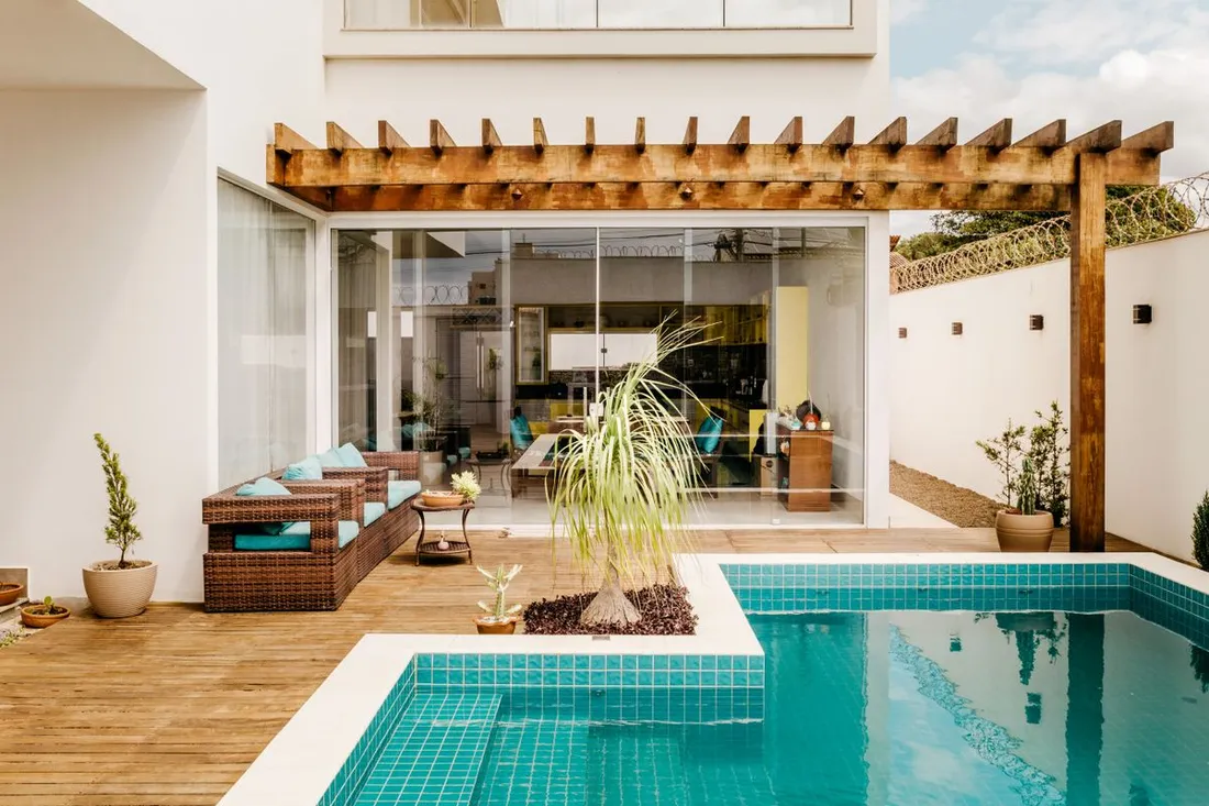 Terrasse en bois et piscine d'une villa de location tropicale avec pergola, salon d'extérieur et baies vitrées ouvertes sur le séjour