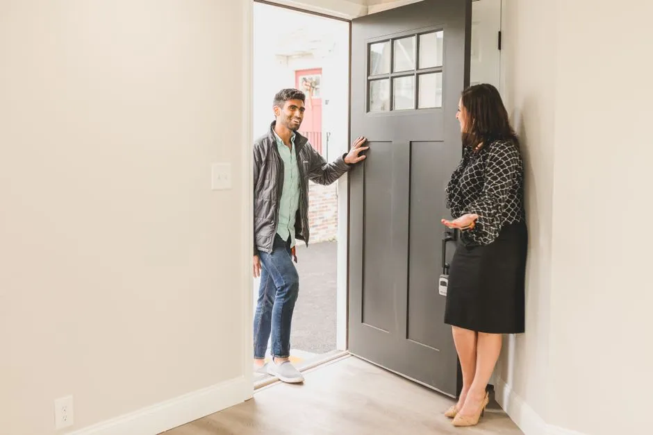 Une hote accueille un visiteur a la porte d'un logement, illustrant la prise en charge des arrivees par une conciergerie