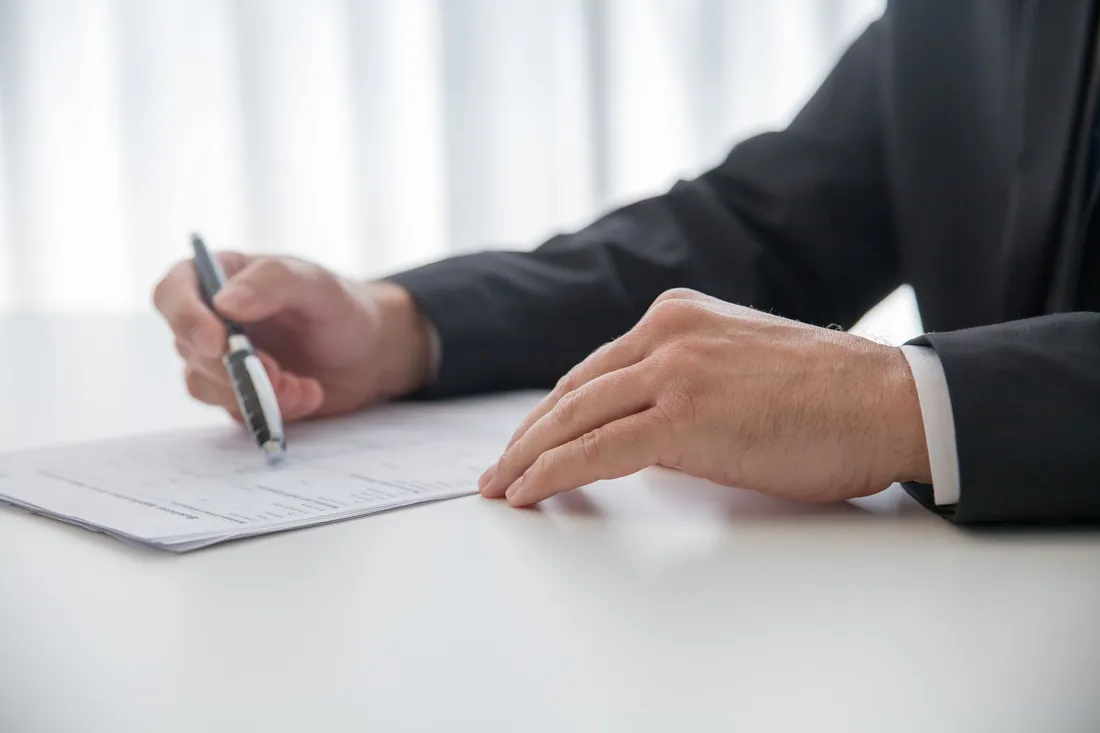 Cadre en costume signant des documents contractuels avec un stylo, sur un bureau clair