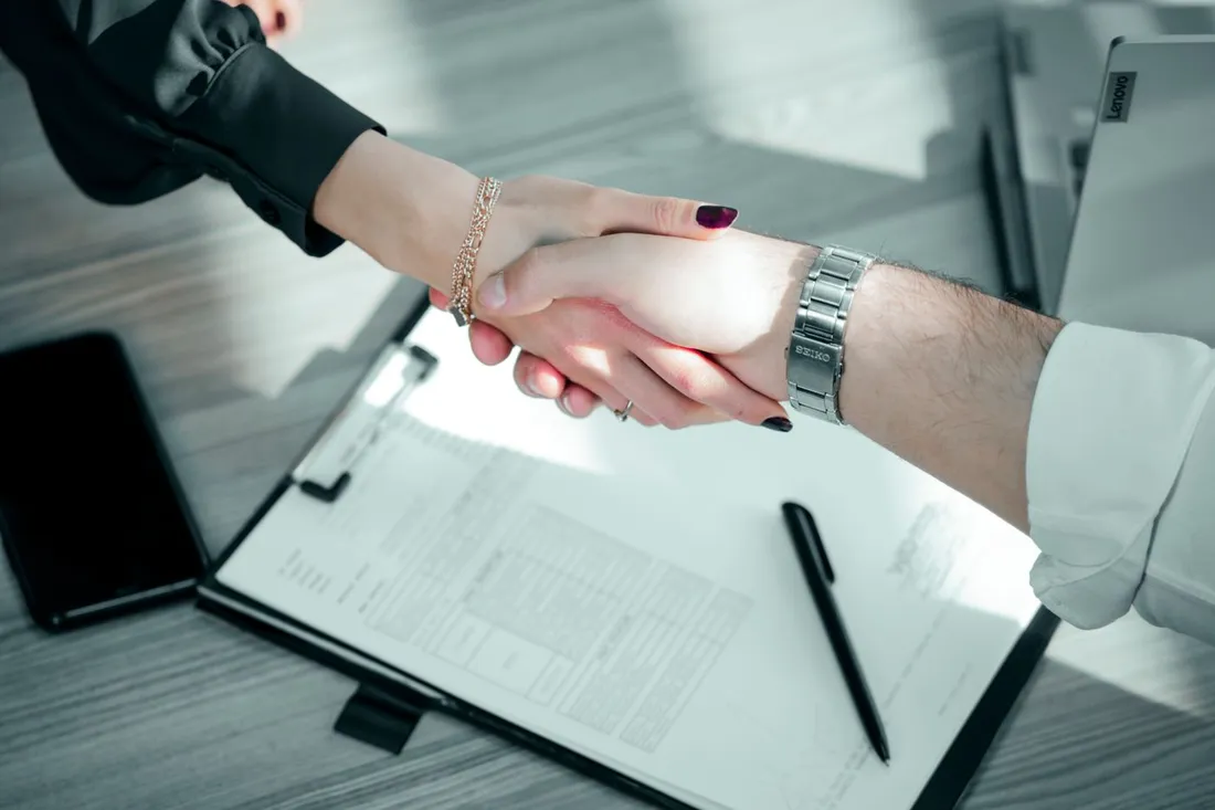 Poignee de main professionnelle au-dessus d'un contrat pose sur un bureau, avec stylo et ordinateur portable