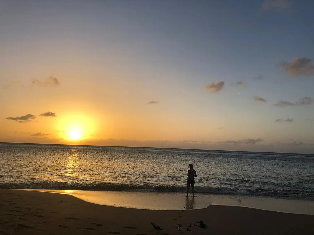 Coucher de soleil sur la mer des Caraïbes à la plage de la Perle à Deshaies, sur la côte sous-le-vent de la Guadeloupe, avec une silhouette au bord de l'eau