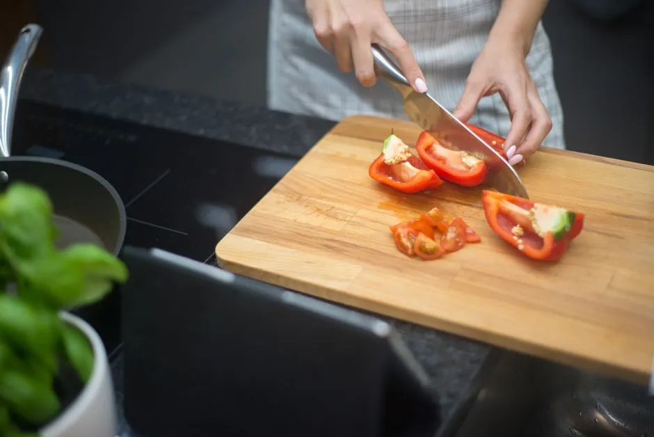 Mains preparant un plat lors d'un cours de cuisine : decoupe de tomates et poivrons sur une planche en bois avec du basilic frais