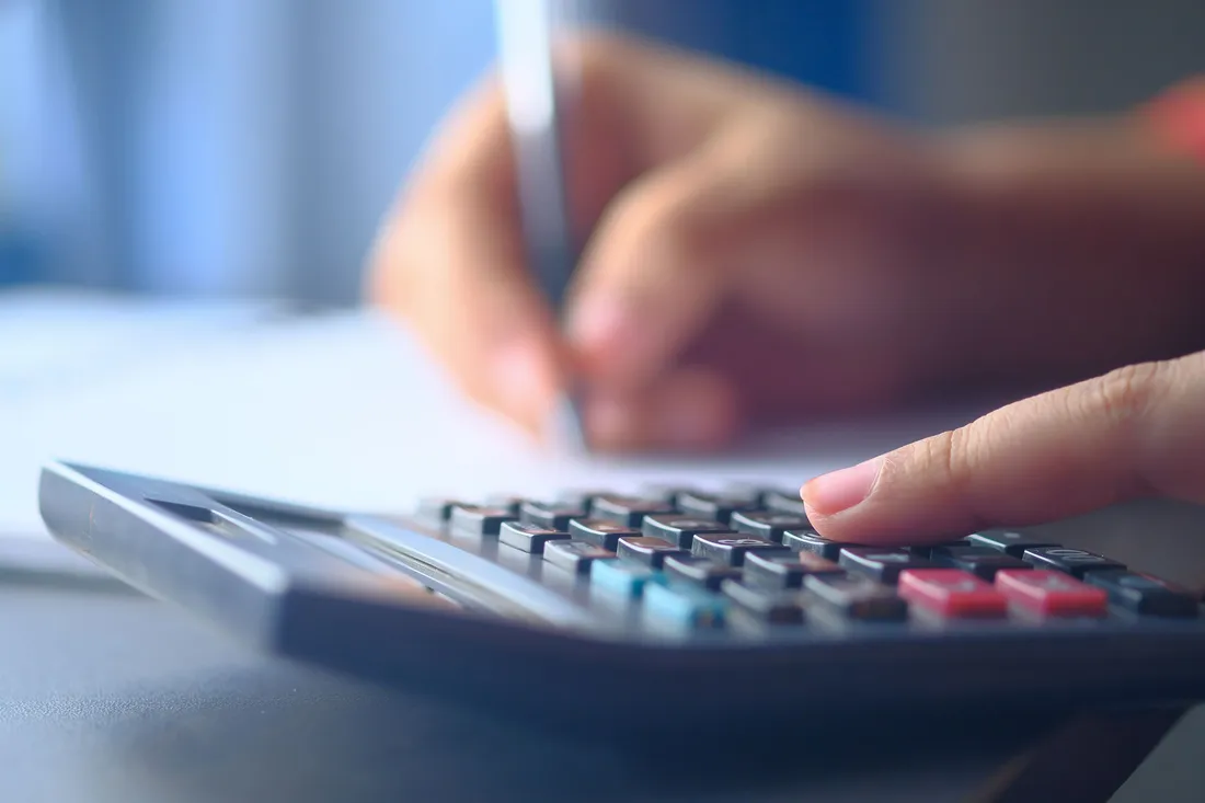 Mains posant les chiffres d'un budget mensuel sur une calculatrice avec un stylo et une feuille