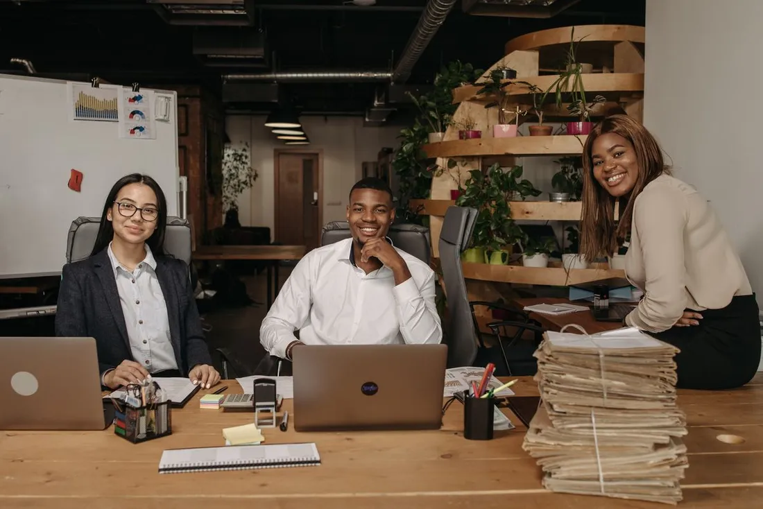 Equipe de professionnels souriants au travail sur des ordinateurs portables dans un bureau lumineux