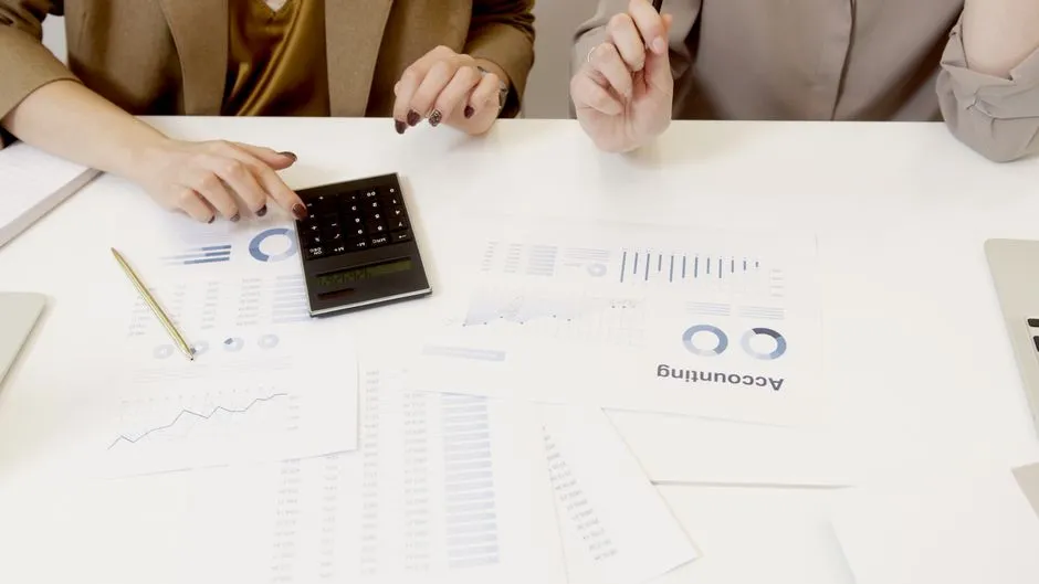 Deux professionnelles calculant un budget à l'aide d'une calculatrice et de tableaux chiffrés étalés sur un bureau
