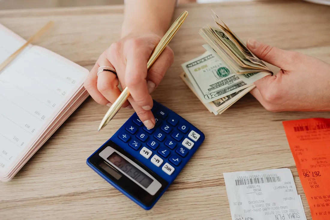 Mains comptant des billets avec une calculatrice, un carnet et des tickets de caisse pour estimer un budget