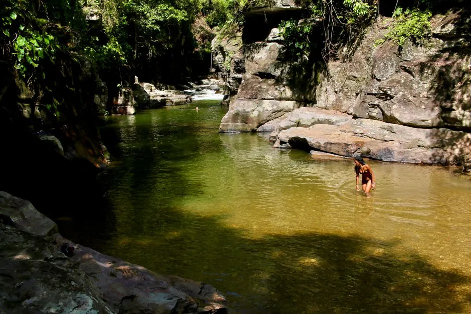 Baigneuse marchant dans l'eau douce et claire d'une crique bordée de rochers et de forêt tropicale