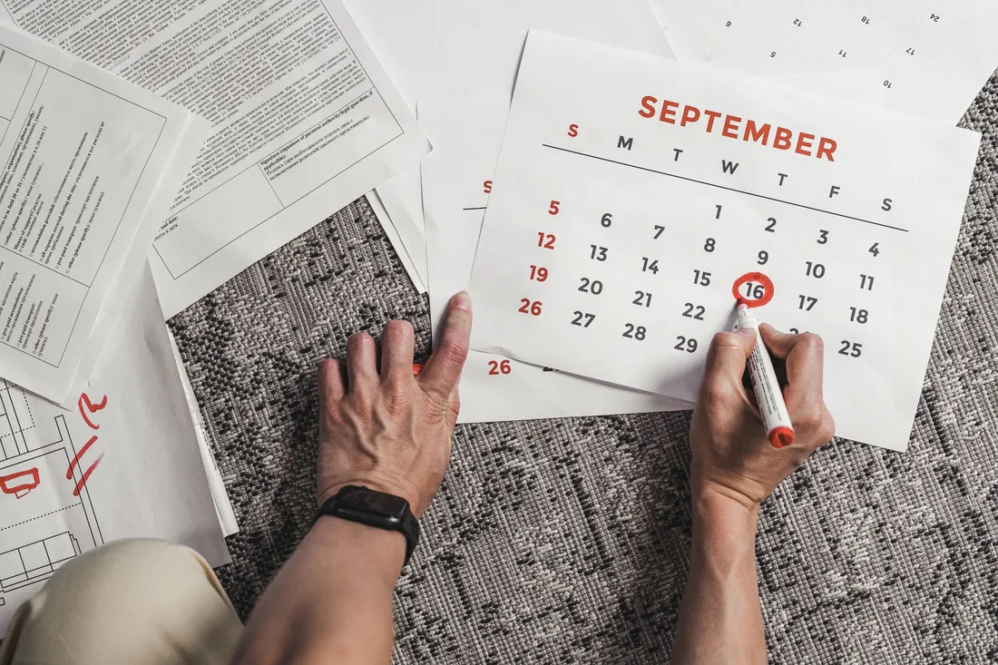 Vue de dessus de deux mains entourant au feutre rouge le 16 septembre sur une page de calendrier, au milieu de formulaires administratifs étalés