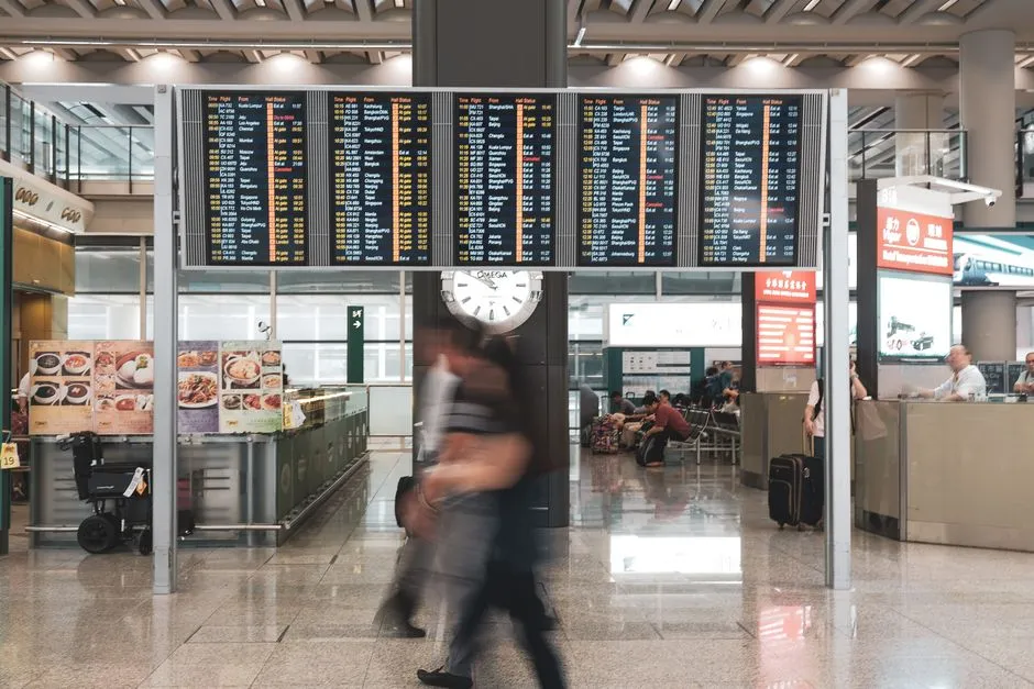 Hall d'aeroport avec horloge et tableaux des horaires de vols, illustrant le decalage horaire et l'organisation de l'arrivee