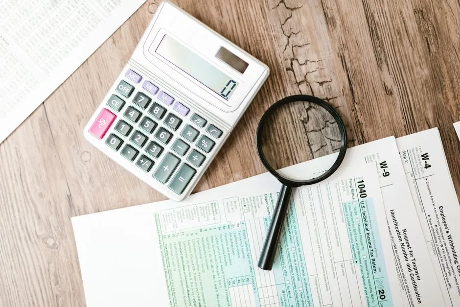 Calculatrice, loupe et formulaires fiscaux posés sur un bureau pour préparer la déclaration des revenus de location meublée