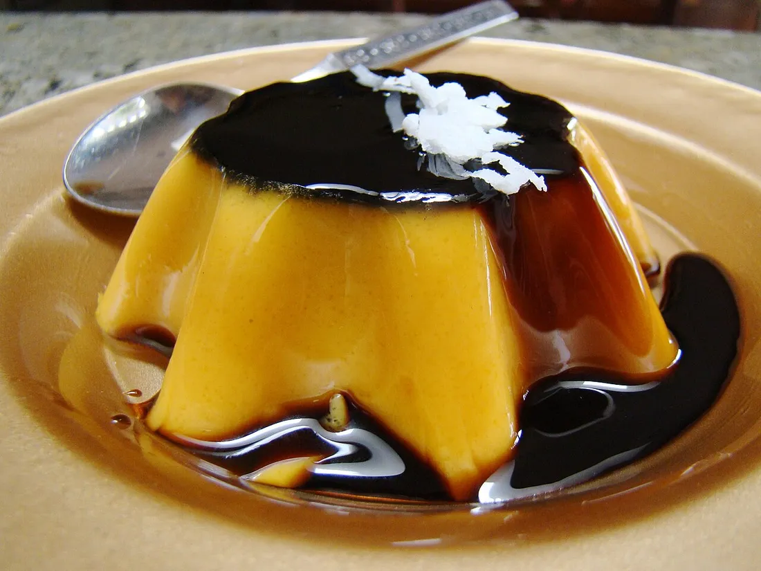 Flan coco nappé de caramel et parsemé de noix de coco rapée, servi dans une assiette avec une cuillere