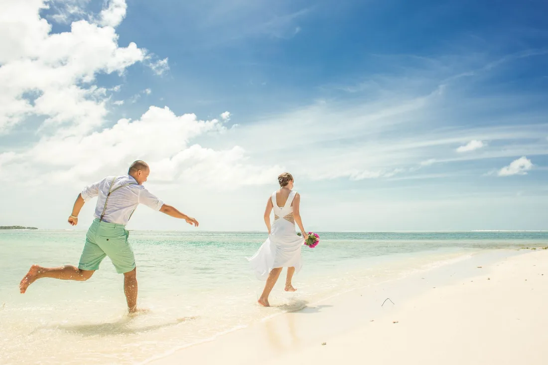 Couple en tenue de mariage courant sur une plage ensoleillée