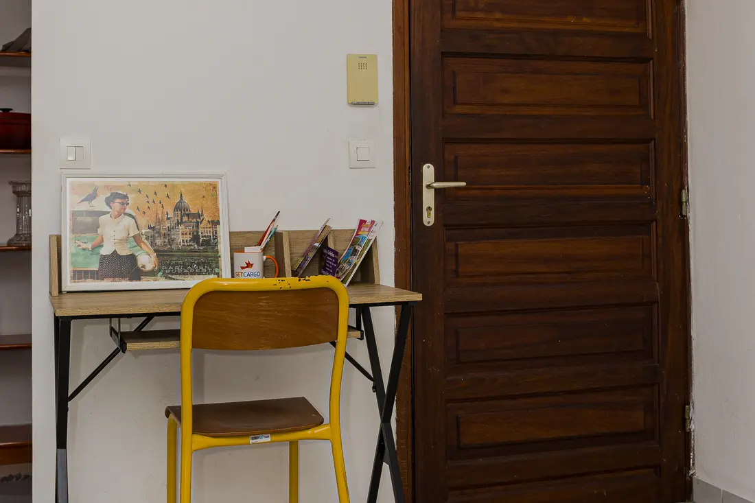 Coin bureau du Cocon Cayennais : petite table en bois à piètement noir, chaise d’écolier jaune et cadre rétro près de la porte en bois