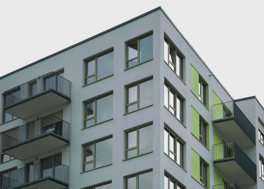 Angle d'un immeuble collectif récent photographié en contre-plongée depuis la rue : façade claire, panneaux vert anis, fenêtres et balcons à garde-corps métalliques