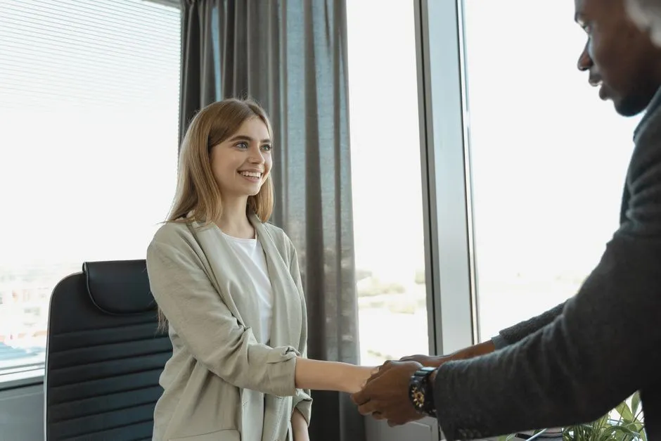 Une candidate souriante serre la main d'un recruteur dans un bureau à l'issue d'un entretien d'embauche