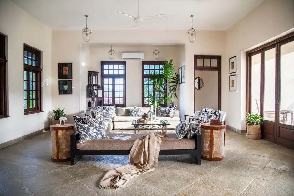 Salon d'un logement de tourisme tropical equipe d'un ventilateur de plafond, d'une climatisation murale, de mobilier en rotin et de larges fenetres ouvertes pour la ventilation