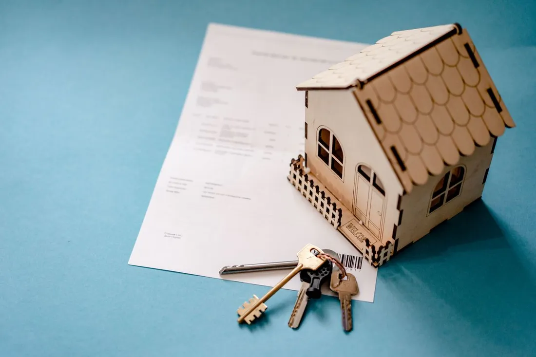 Maquette de maison en bois posée à côté d'un trousseau de clés et d'un contrat, illustrant l'achat d'un investissement locatif