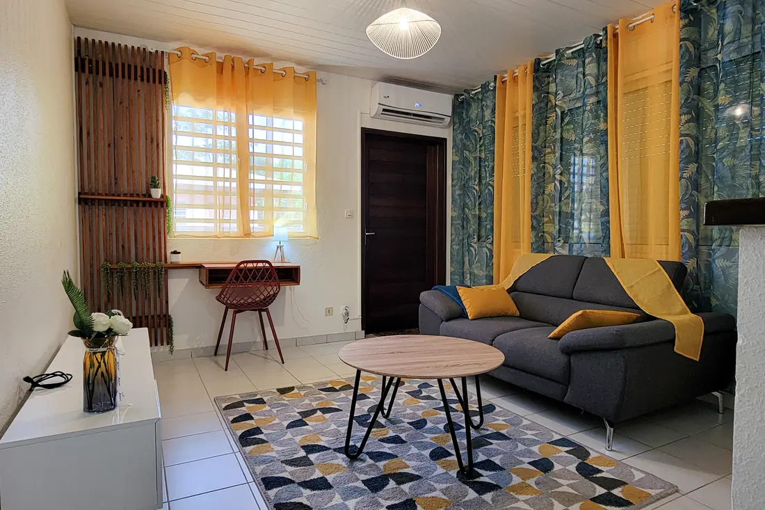 Sala de um apartamento Cayenne Chic com sofá, mesa de centro e cortinas claras
