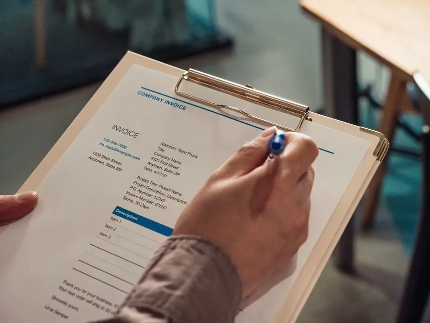 Main remplissant au stylo une facture d'entreprise pré-imprimée fixée sur un porte-bloc, avec numéro de facture, coordonnées et lignes de prestations