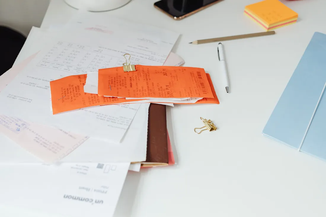 Factures, reçus et documents comptables posés sur un bureau avec stylo et bloc-notes