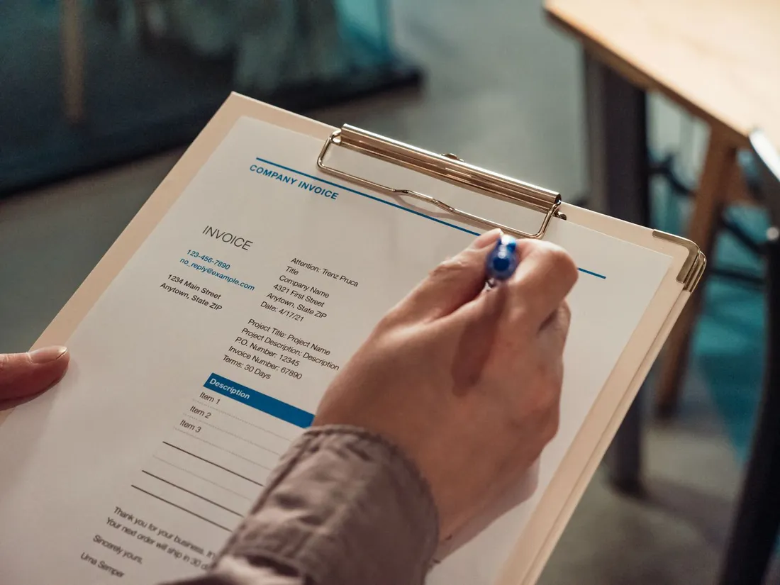 Main tenant une facture professionnelle « Company Invoice » sur une écritoire, avec numéro et mentions détaillées